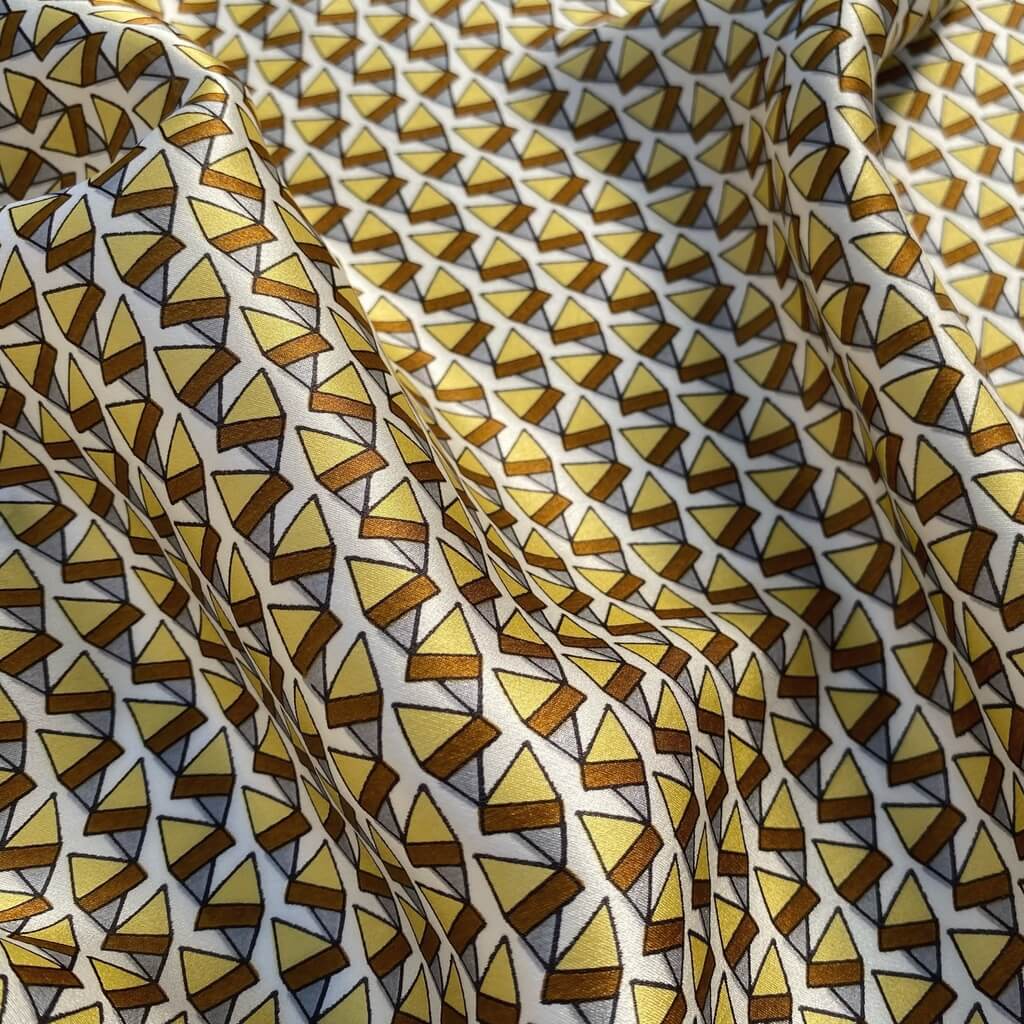 close up of a mulberry silk square scarf with a pattern of brown and yellow triangles on a white background