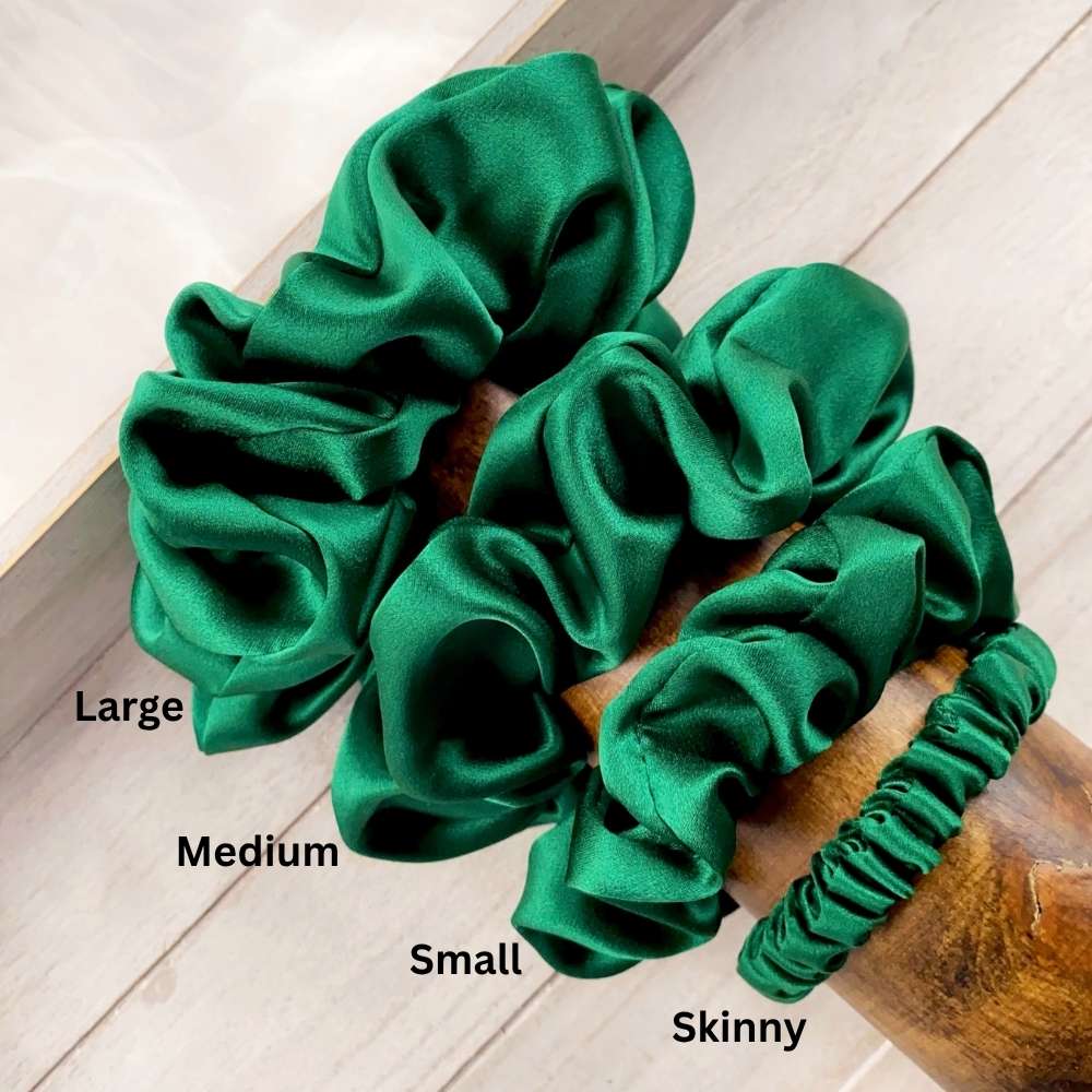 Set of green mulberry silk satin scrunchies with labels for size on a wooden surface