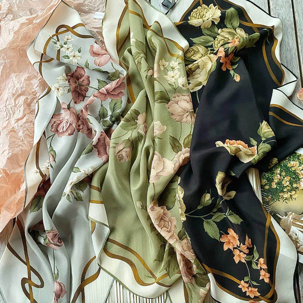 Collection of floral-patterned scarves in light grey, olive green and black colors on a table.