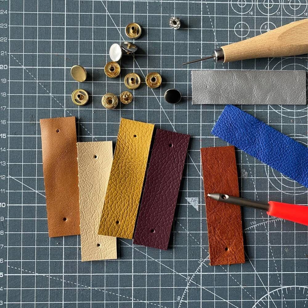Assorted leather strips and tools on a grid surface