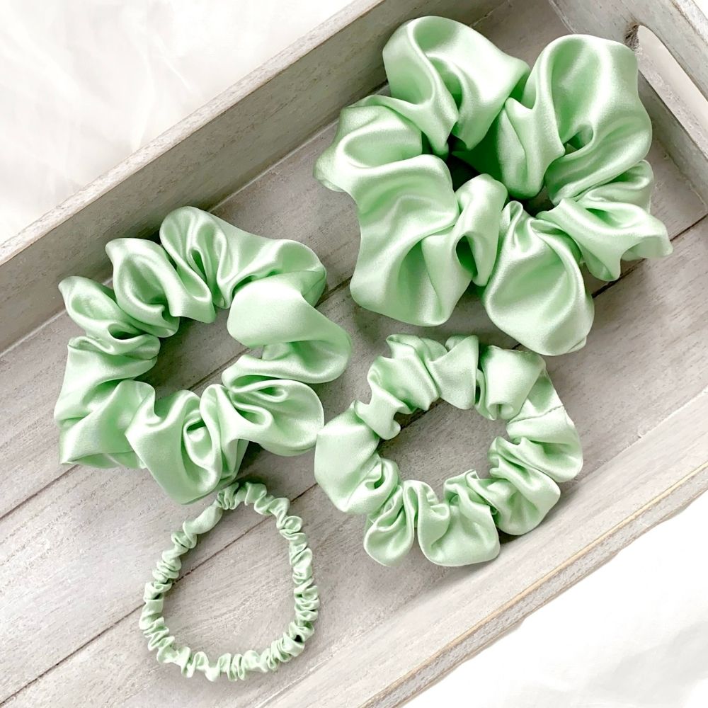 Set of mint green mulberry silk scrunchies and hair ties on a wooden surface