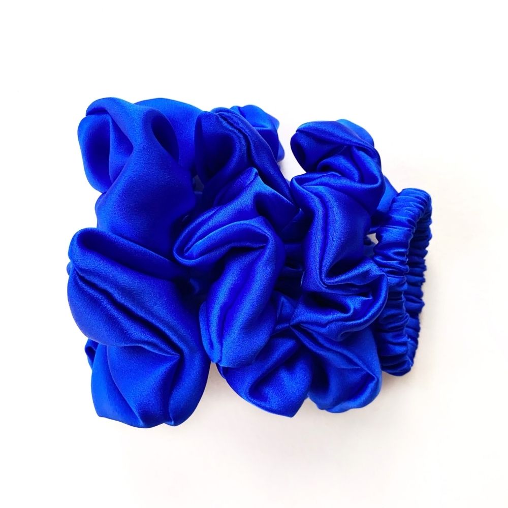 Four royal blue mulberry silk satin scrunchies and silk hair ties on a white background