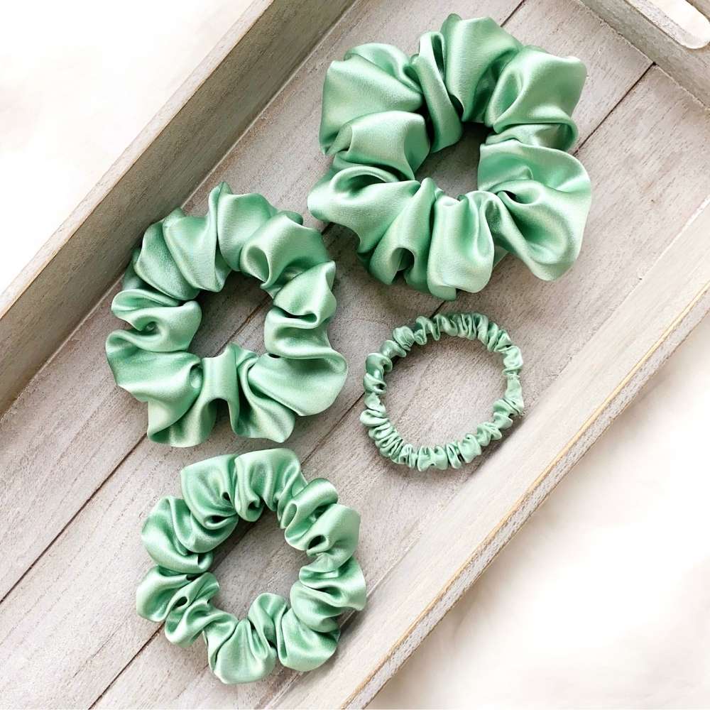 Four mint green mulberry silk scrunchies on a wooden surface