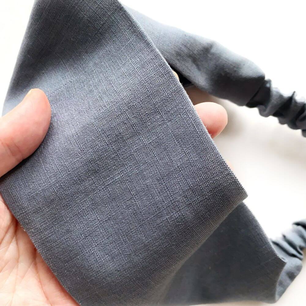 Close-up of a hand holding gray linen headband with a textured surface.