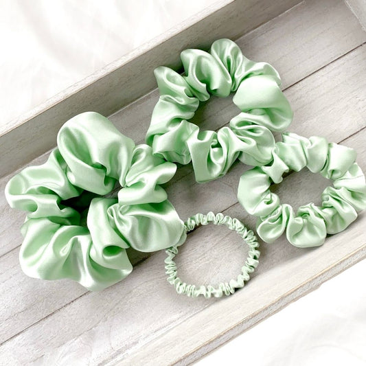 Set of mint green mulberry silk scrunchies and hair ties on a wooden surface