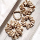 Four beige khaki silk satin scrunchies hair ties on a light wooden surface