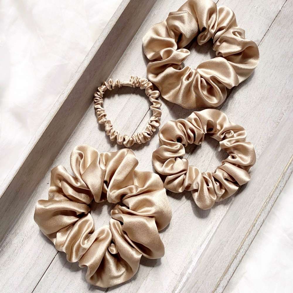 Four beige khaki silk satin scrunchies hair ties on a light wooden surface