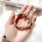 beige khaki silk satin hair tie held in a hand on a light background