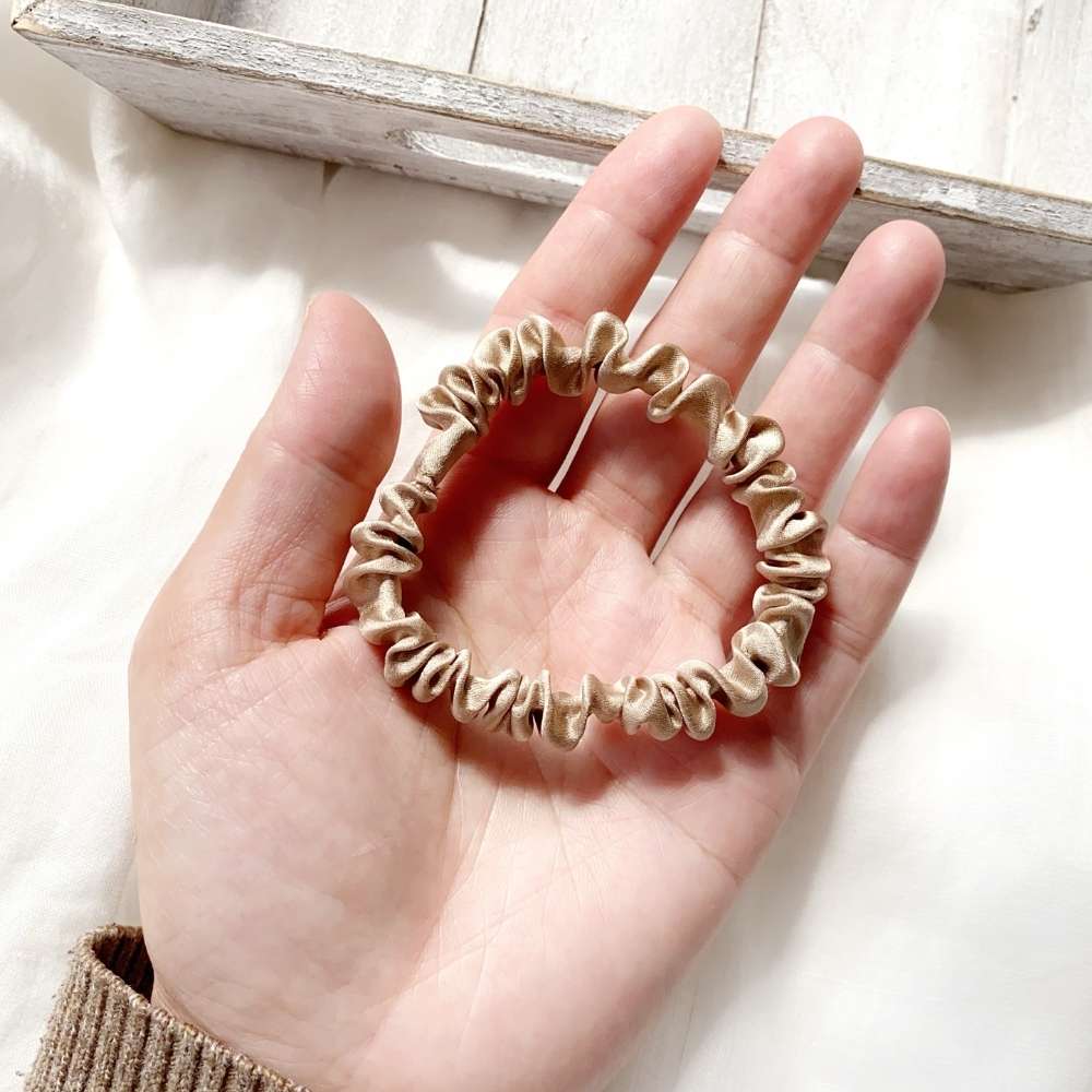 beige khaki silk satin hair tie held in a hand on a light background