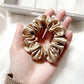 beige khaki silk satin scrunchie held in a hand with a light background