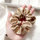 beige khaki silk satin scrunchie held in a hand against a neutral background