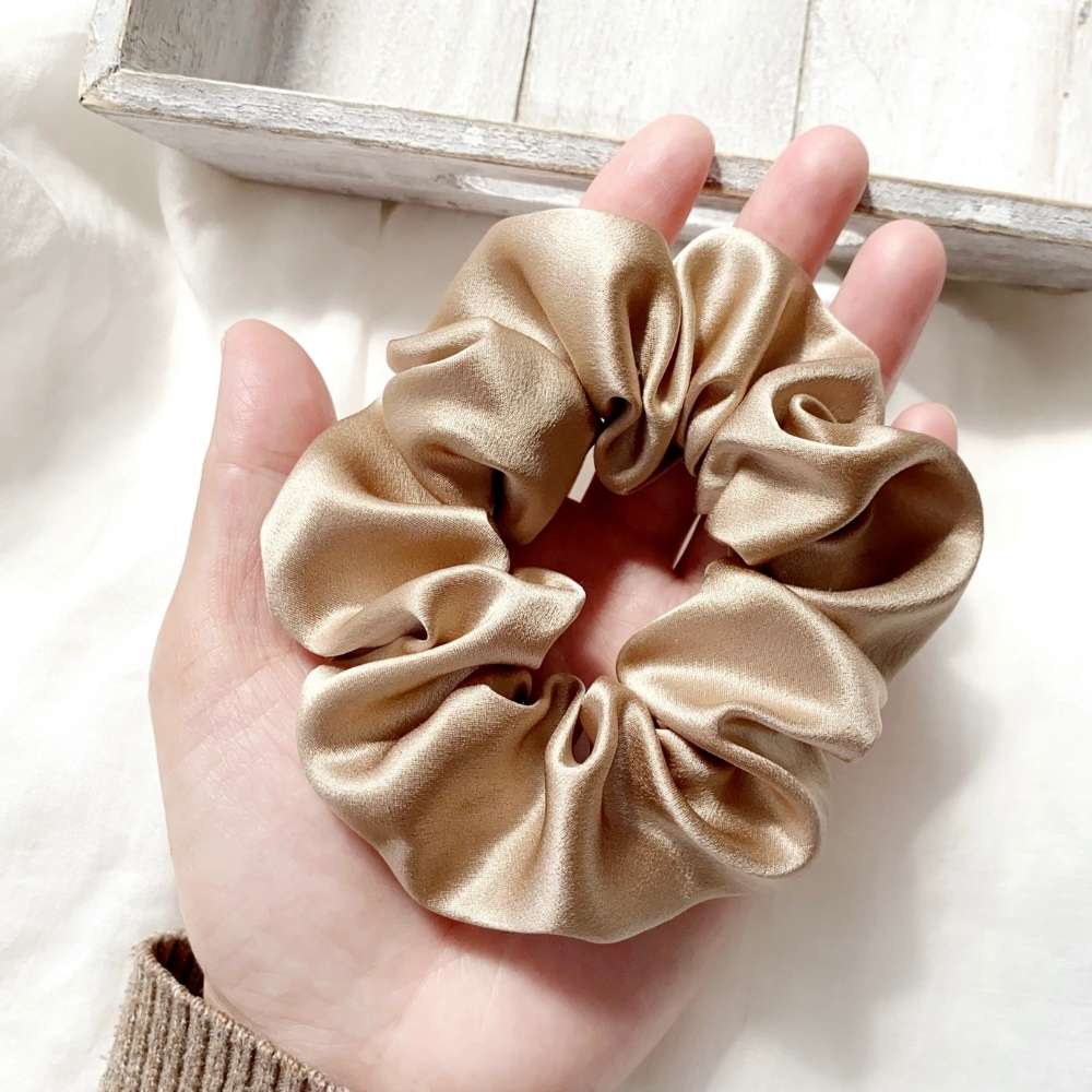 beige khaki silk satin scrunchie held in a hand against a neutral background