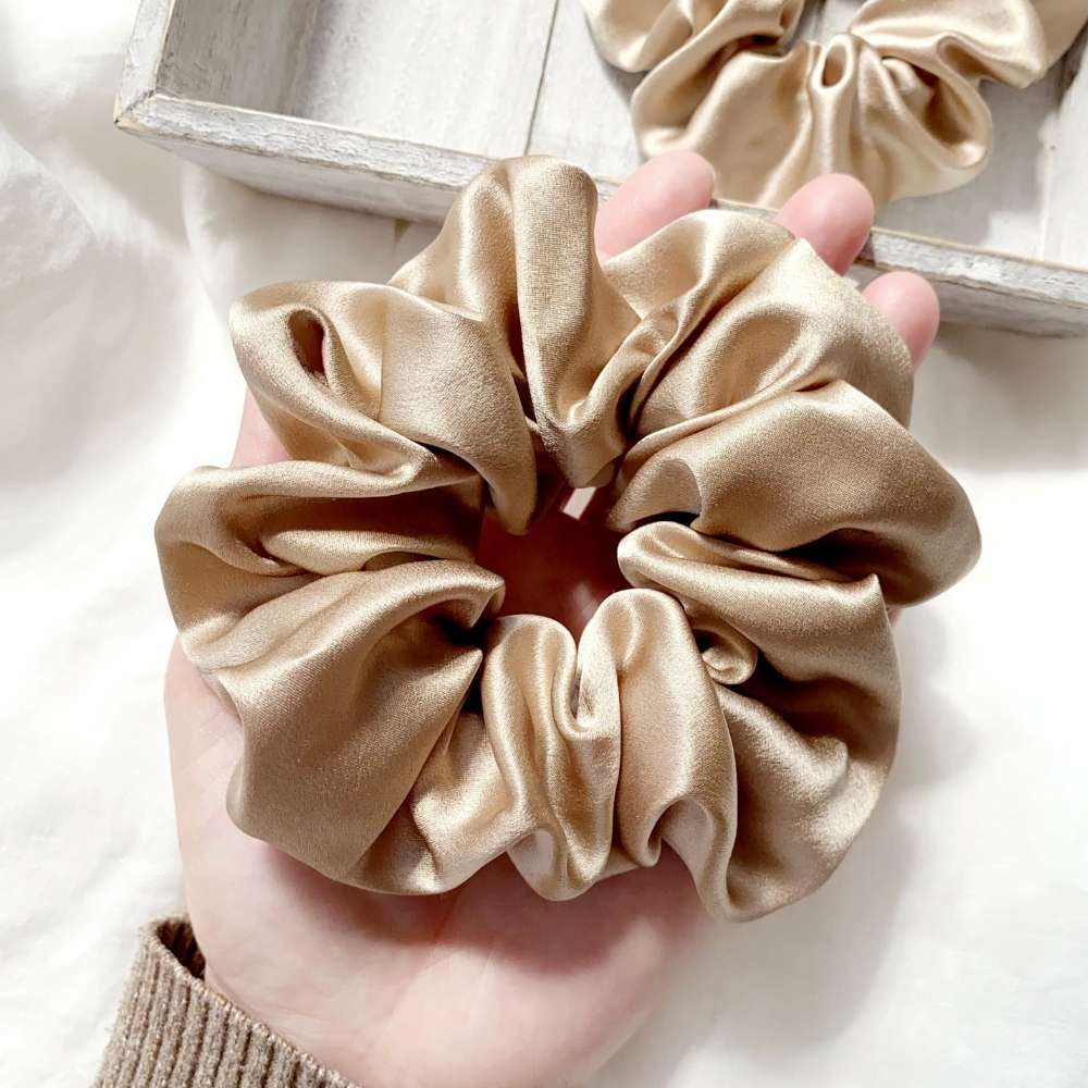beige khaki silk satin scrunchie held in a hand with a blurred background