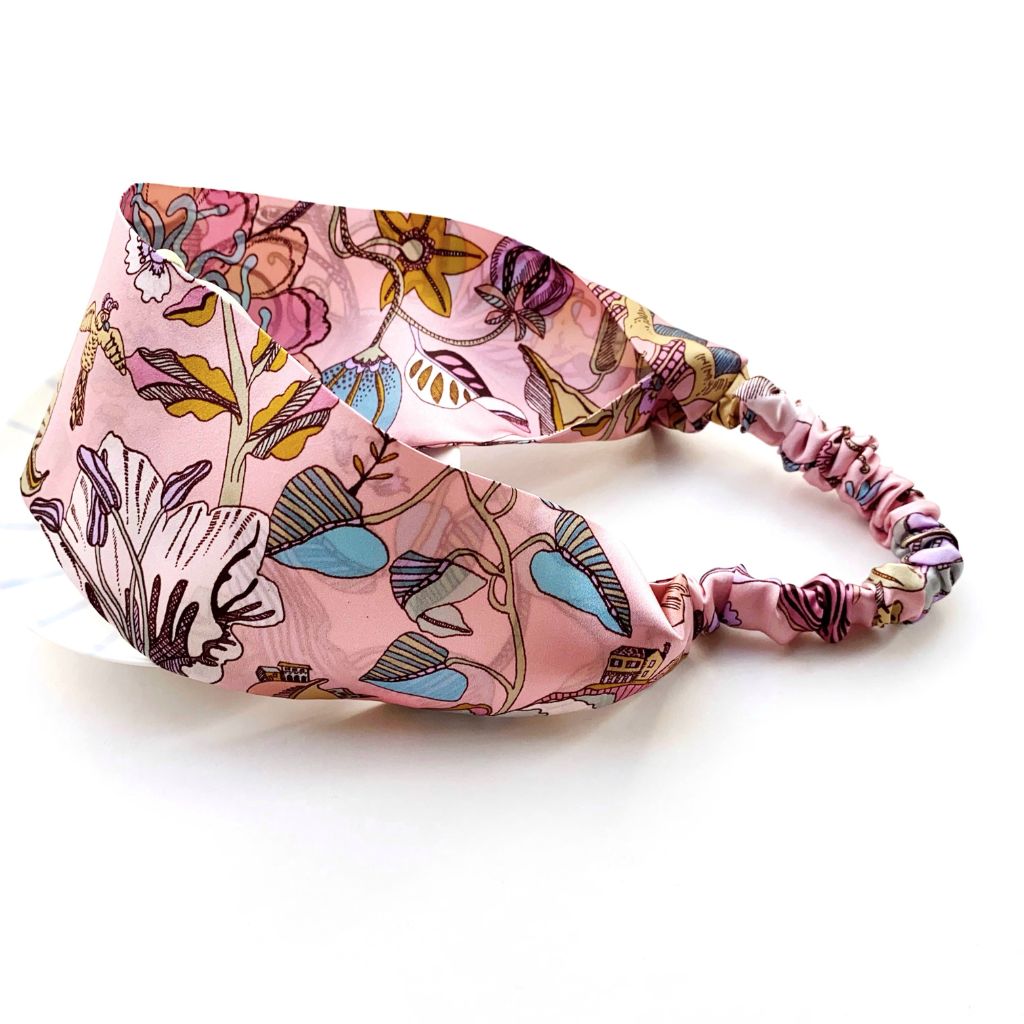 A pink  Liberty London mulberry silk satin headband with a colorful floral pattern, featuring an elastic band back shown on a white background.