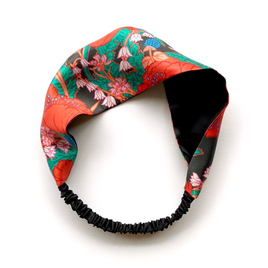 A Liberty London mulberry silk satin headband with a vibrant floral and botanical print in red, green, pink, and black, featuring a black elasticized band at the bottom, shown on a plain white background.
