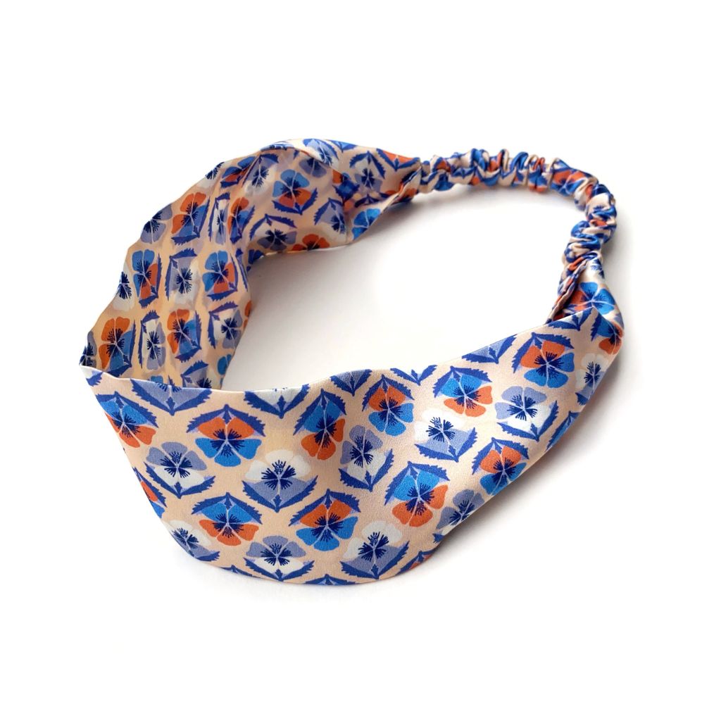 A  Liberty London mulberry silk satin headband with a geometric pattern in blue, orange, and beige, photographed on a clean white background.