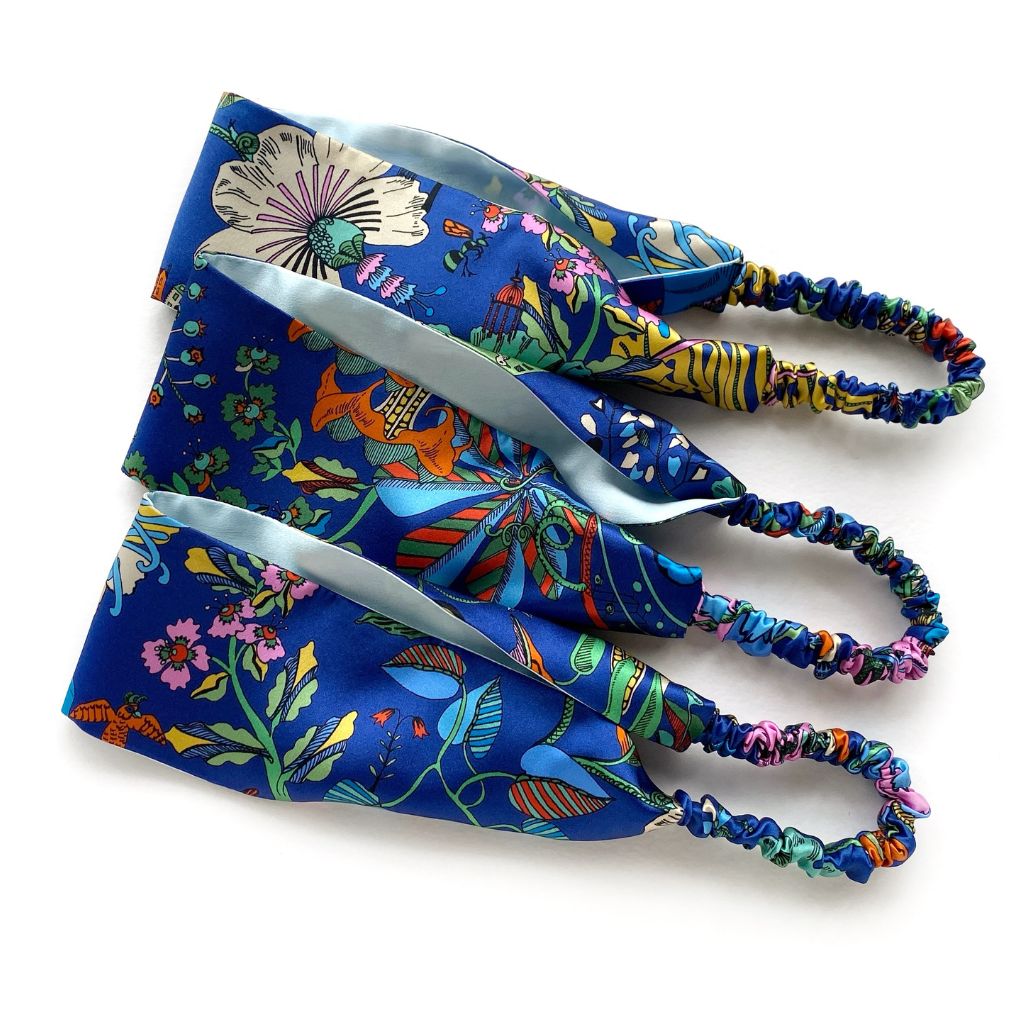 Three  Liberty London mulberry silk satin headbands with colorful  prints on a blue background, arranged diagonally on a white background.