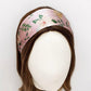 A wide pink  Liberty London mulberry silk satin headband with a floral print, displayed on a mannequin head with brown hair against a plain white background.