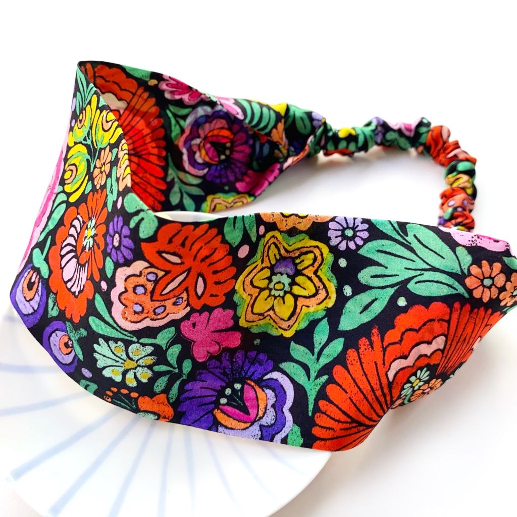 A colorful floral  Liberty London mulberry silk satin headband with a black background and vibrant multicolor flowers, displayed on a white surface.