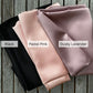 Three folded mulberry silk fabrics in black, pastel pink, and dusky lavender on a wooden surface.
