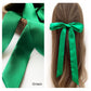 A green mulberry silk satin skinny ribbon scarf tied as a hairbow, styled against a crisp white background.