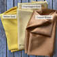 Three folded mulberry silk fabric swatches labeled 'Yellow Gold', 'Champagne Gold', and 'Copper Brown' on a wooden background.