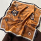 Amber-coloured mulberry silk square scarf with a compass print, laid flat against a white background.