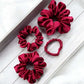 Set of red silk satin hair scrunchies on a light wooden surface