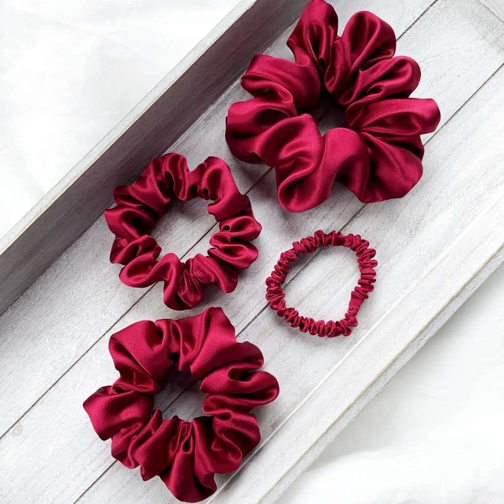 Set of red silk satin hair scrunchies on a light wooden surface