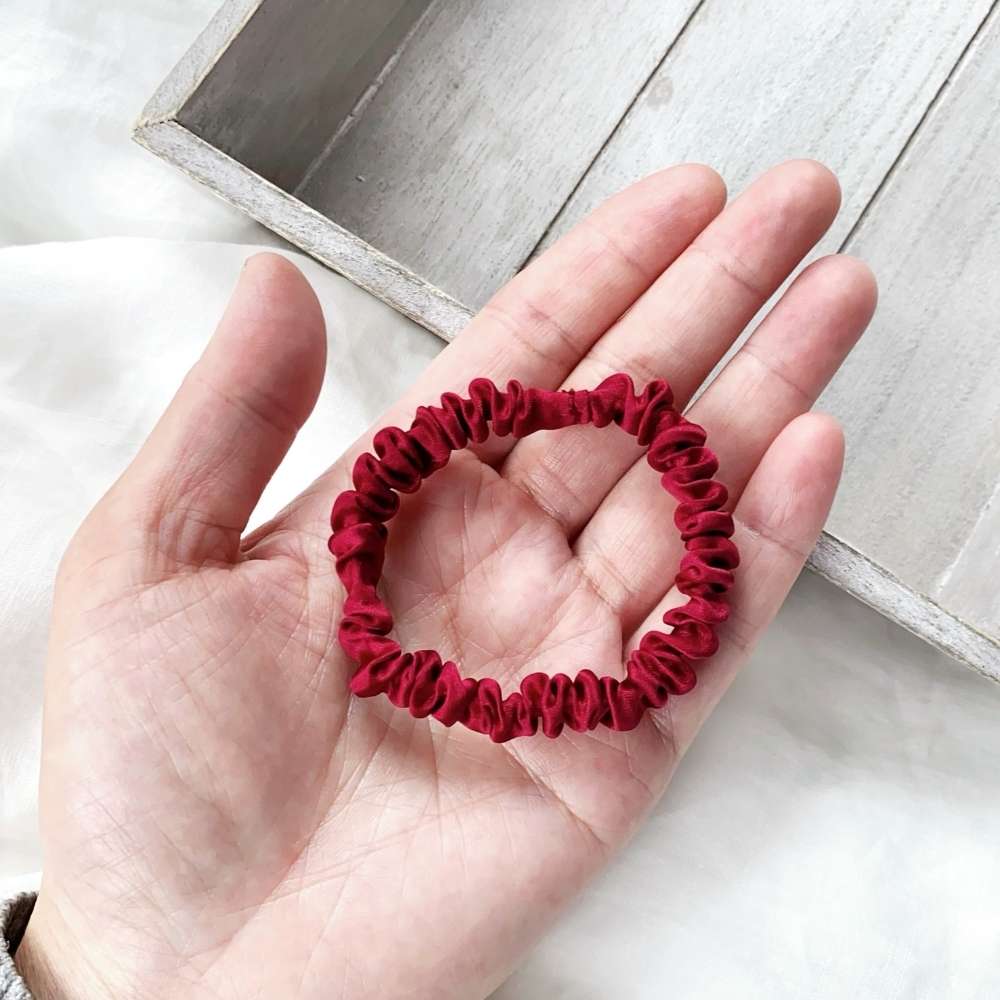Red silk hair tie held in a hand on a light wooden surface