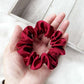 Red silk scrunchie held in a hand on a light wooden surface