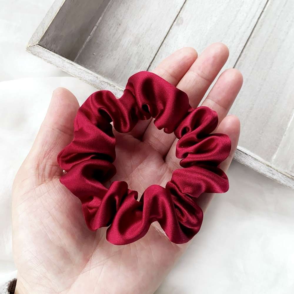 Red silk scrunchie held in a hand on a light wooden surface