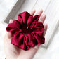 Red silk scrunchie held in a hand on a light wooden surface