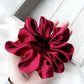Red silk scrunchie held in a hand on a light wooden surface