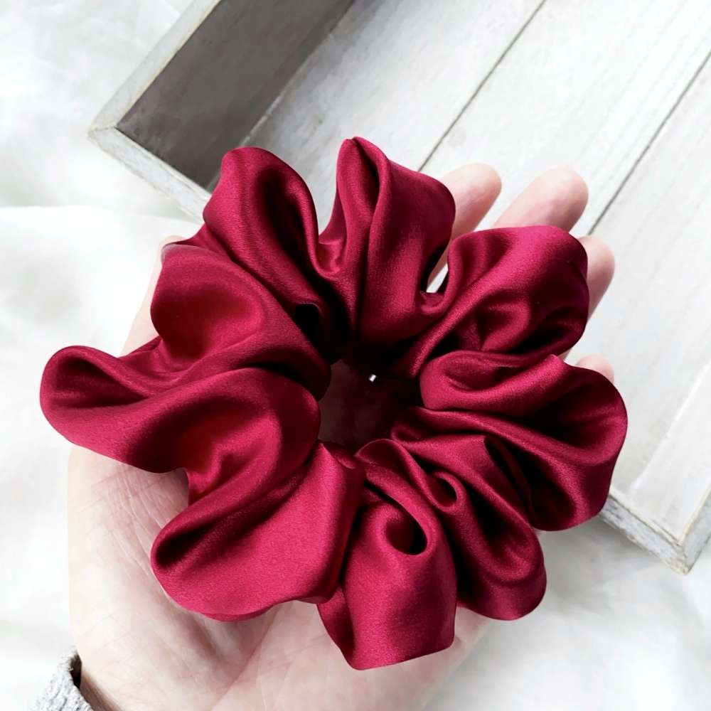 Red silk scrunchie held in a hand on a light wooden surface