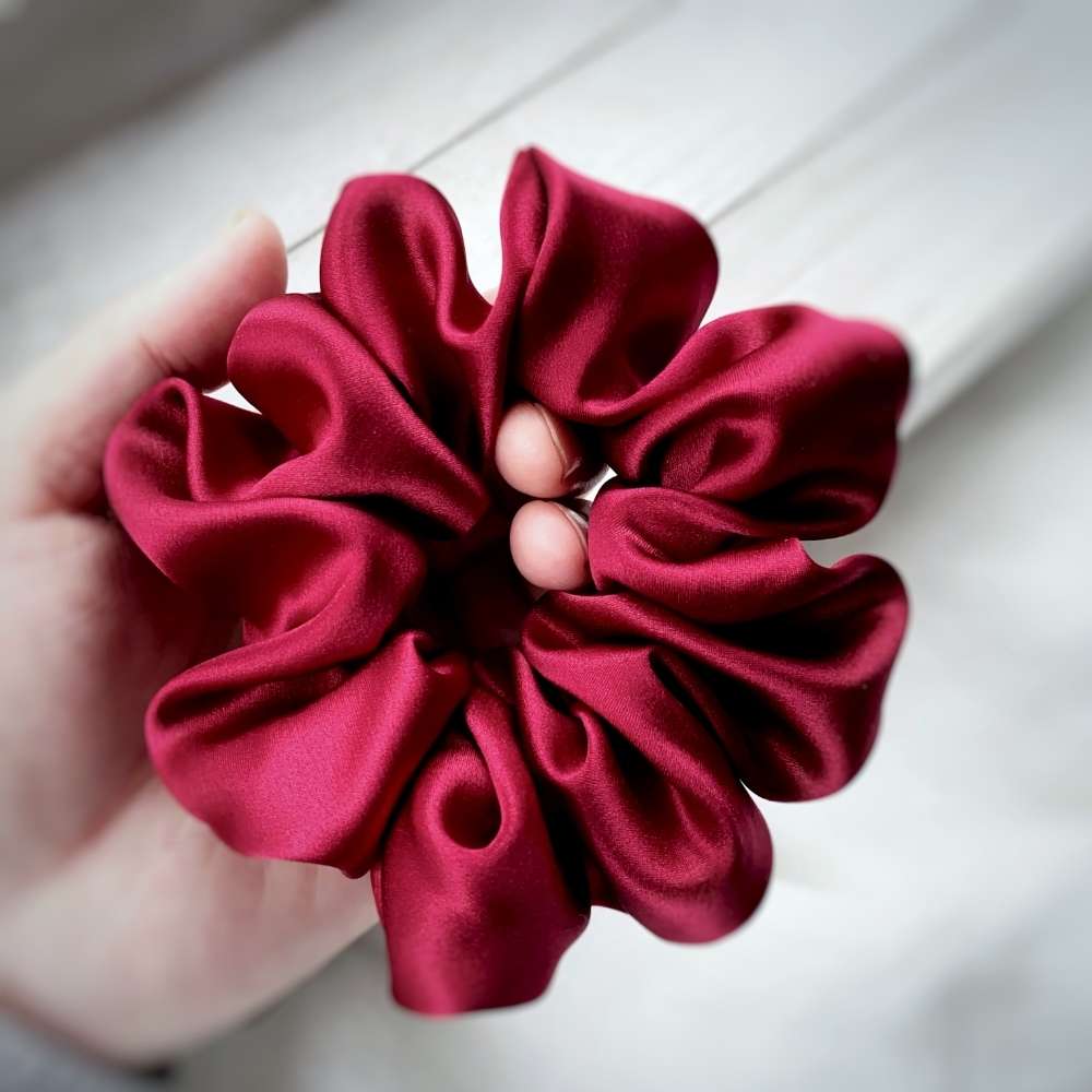 Red scrunchie held in a hand against a light wooden background