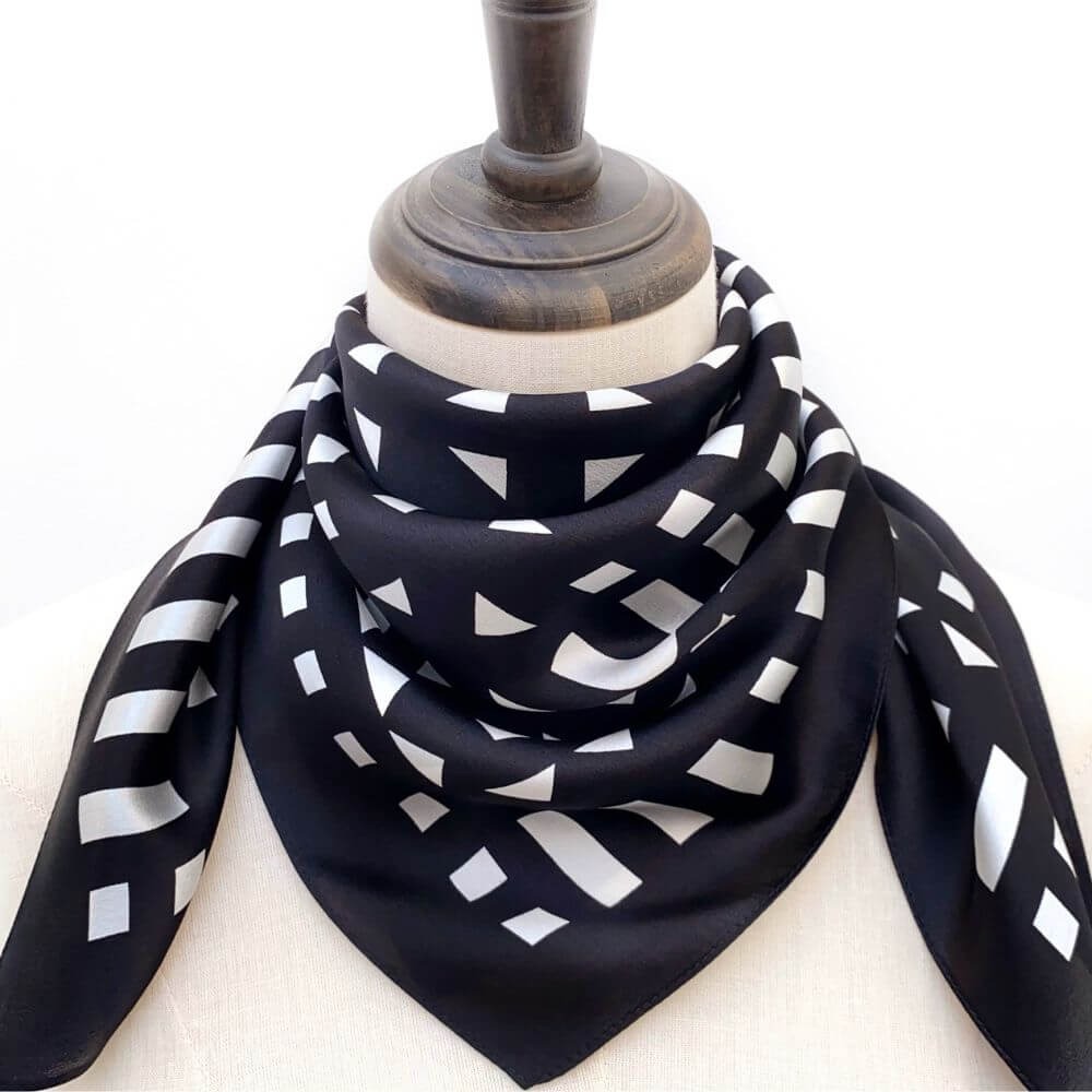Black and white geometric patterned silk scarf on a mannequin with a white background