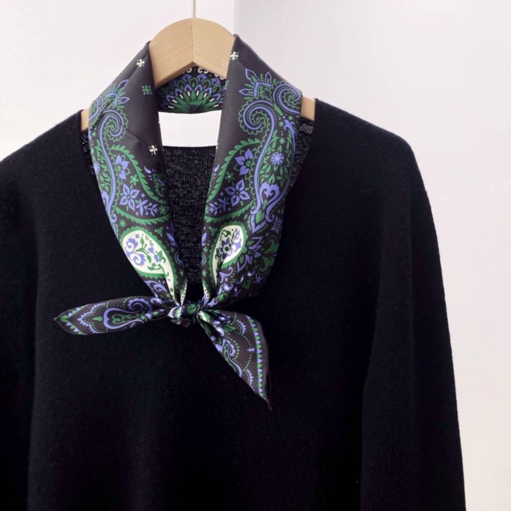 Black sweater with a green and purple paisley patterned mulberry silk neck scarf on a mannequin against a white background