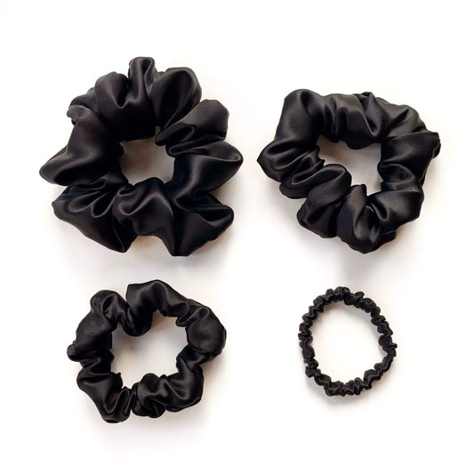 Four black mulberry silk scrunchies and hair ties on a white background