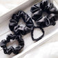 Black mulberry silk satin scrunchies and hair ties  on a light wooden surface