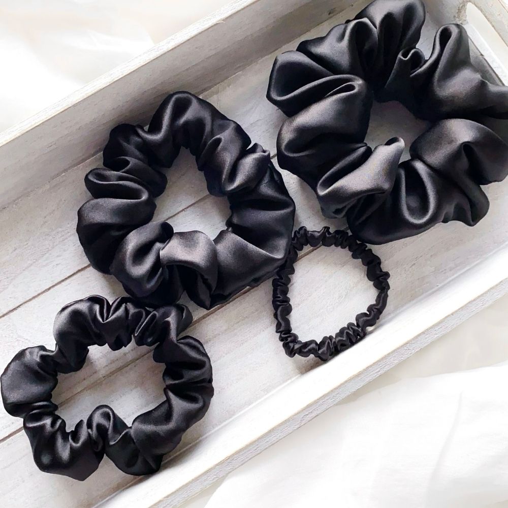Black mulberry silk satin scrunchies and hair ties  on a light wooden surface