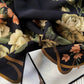 A close-up of a draped mulberry silk crepe de chine scarf featuring a dark navy background with large cream and beige flowers, green leaves, and peach-orange blossoms, plus metallic gold curved accents.