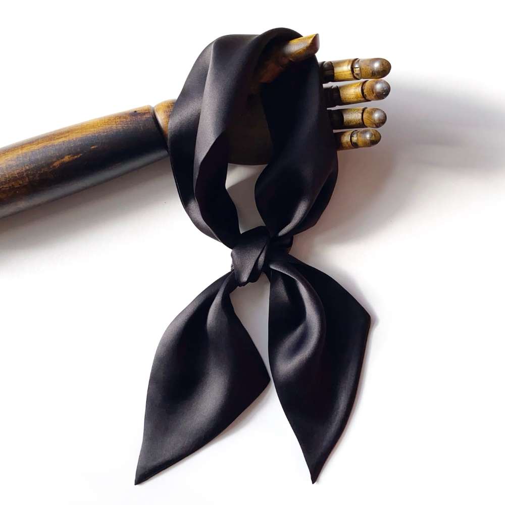 Black mulberry silk satin scarf tied around a wooden hand on a white background