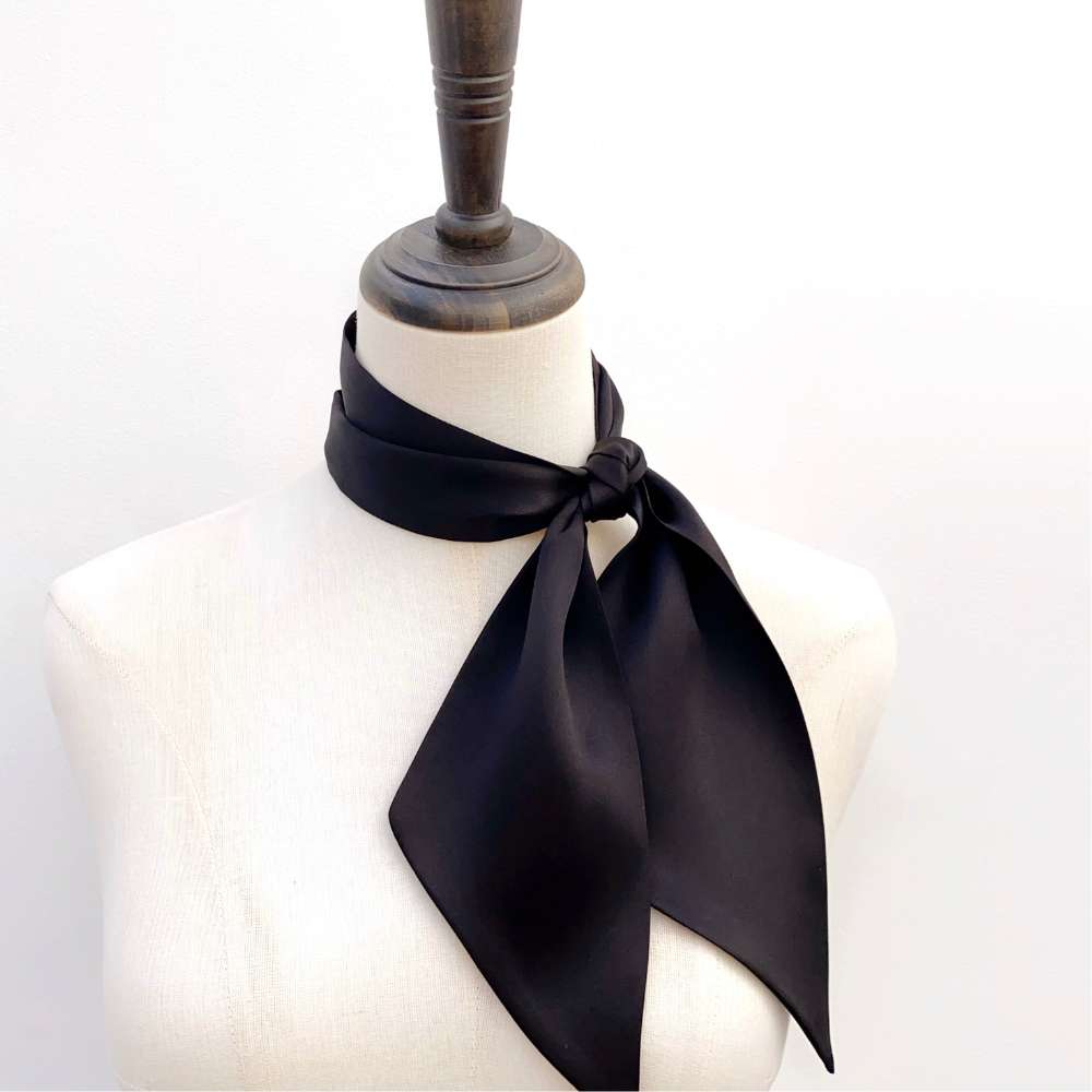 Black long silk scarf tied around a mannequin neck on a white background