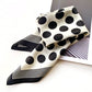 Black and white polka dot silk scarf with striped pattern on a white surface