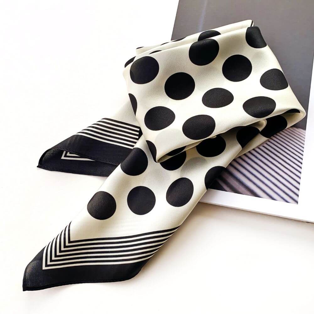 Black and white polka dot silk scarf with striped pattern on a white surface