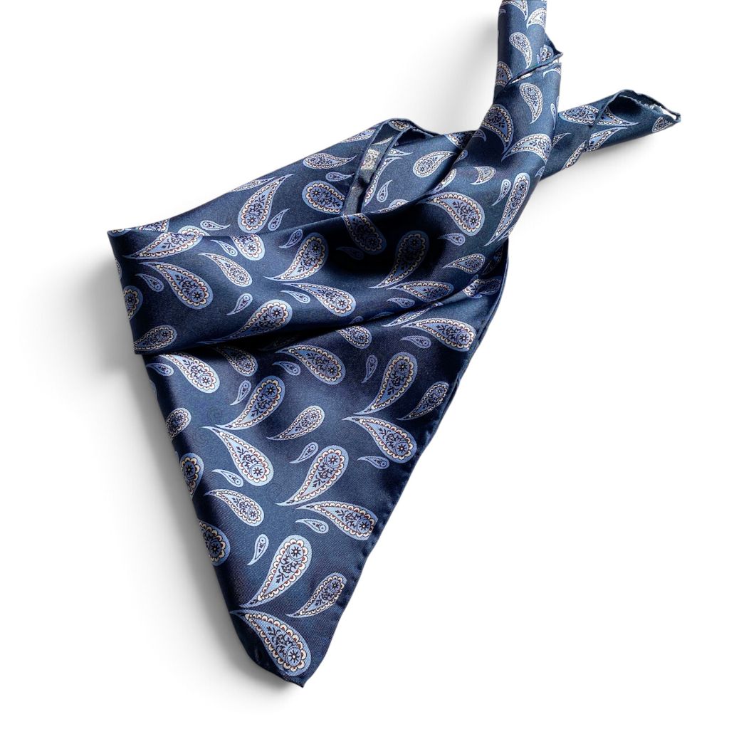 Blue paisley print mulberry silk square scarf tied into a triangle, placed on a white background