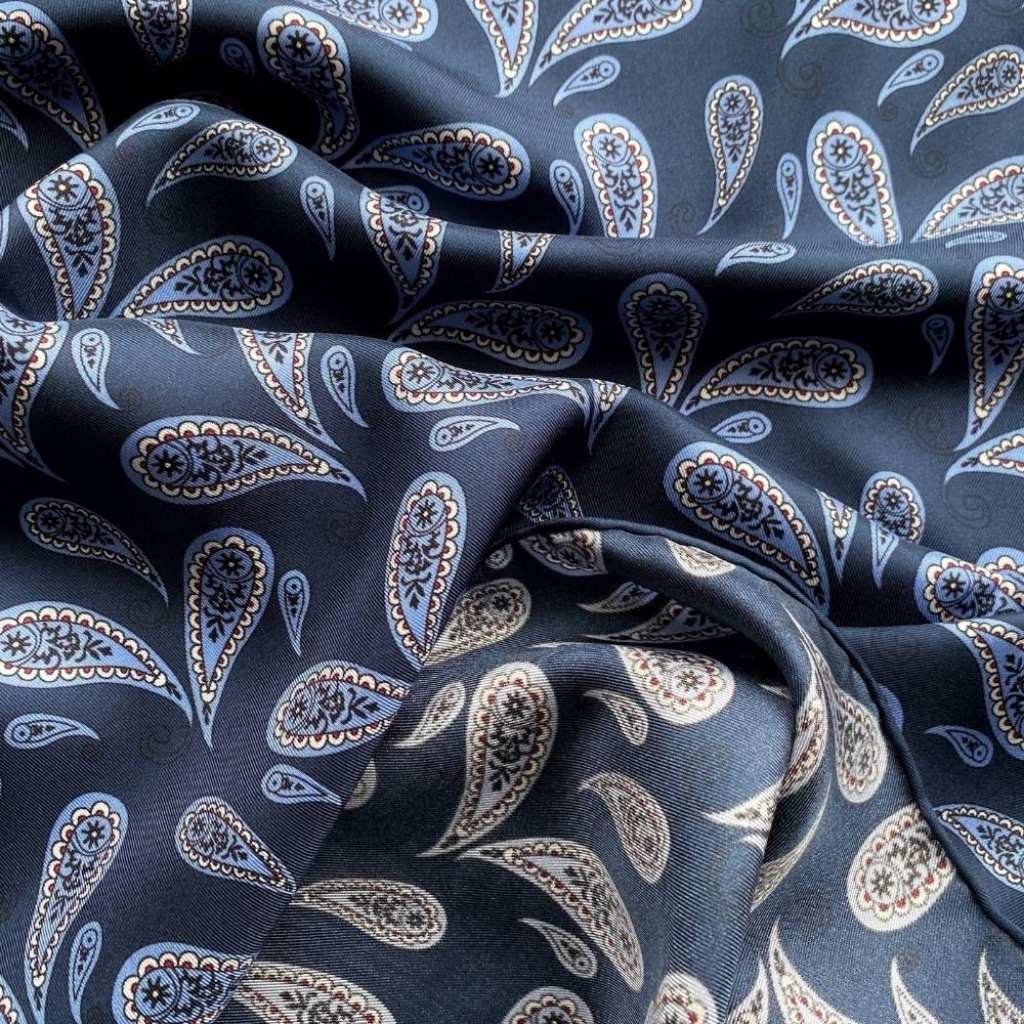 Close-up of a blue paisley print mulberry silk twill square scarf with a hand-rolled hem