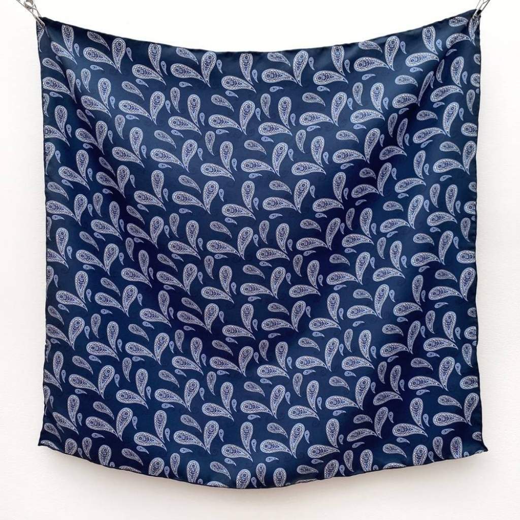 Blue paisley print mulberry silk square scarf hanging on a white wall