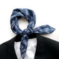 Blue paisley print mulberry silk square scarf tied into a neckerchief, placed around a black blazer and white T-shirt on a white background